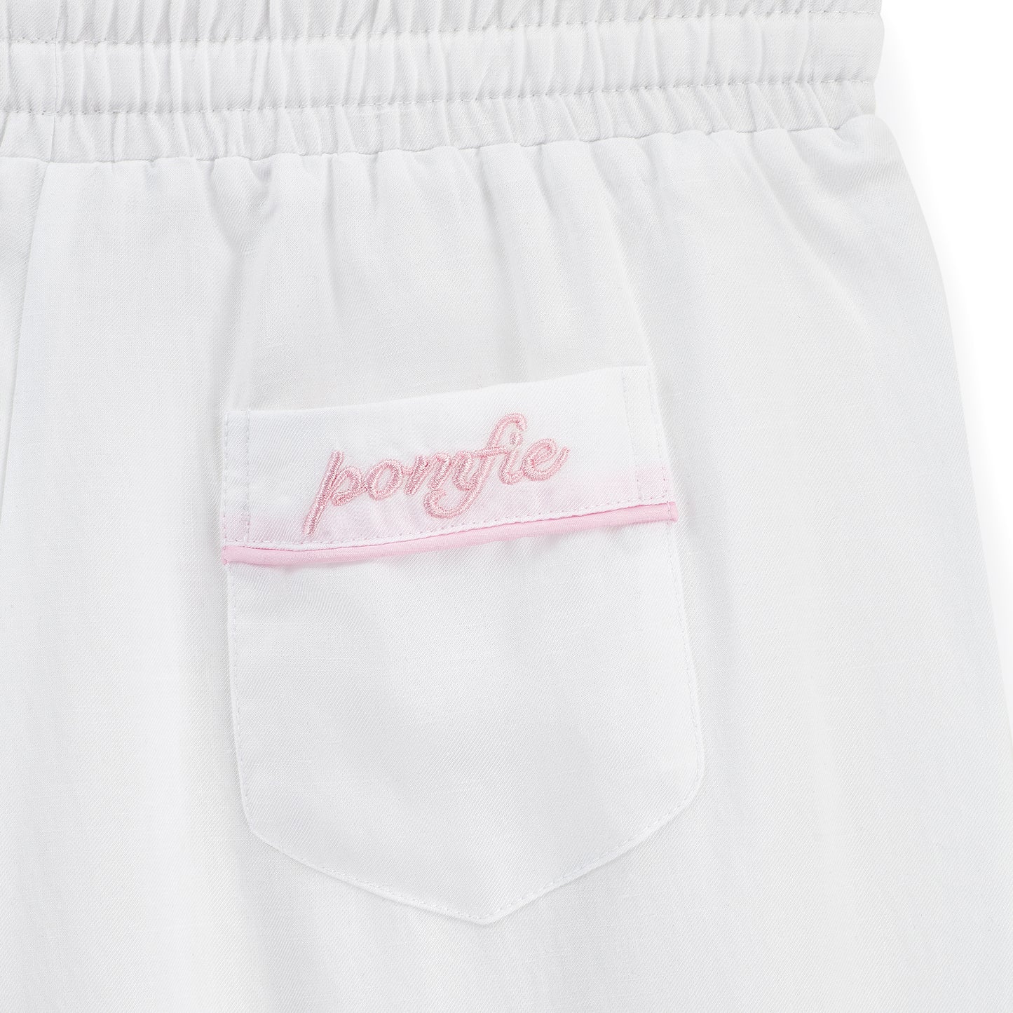 white pyjama pants pocket detail. with baby pink embroidery of pomfie logo and baby pink piping