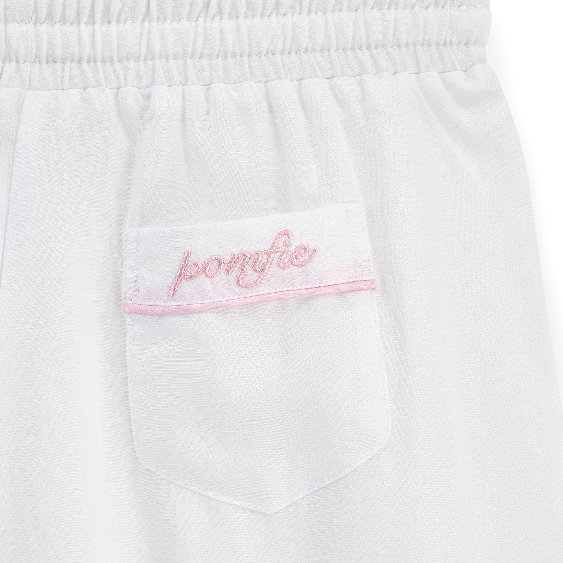 white pyjama pants pocket detail. with baby pink embroidery of pomfie logo and baby pink piping